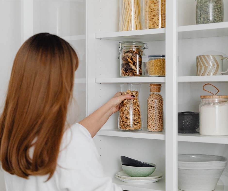 Woman storing pantry items on a shelf. Image credit: Karolina Grabowska