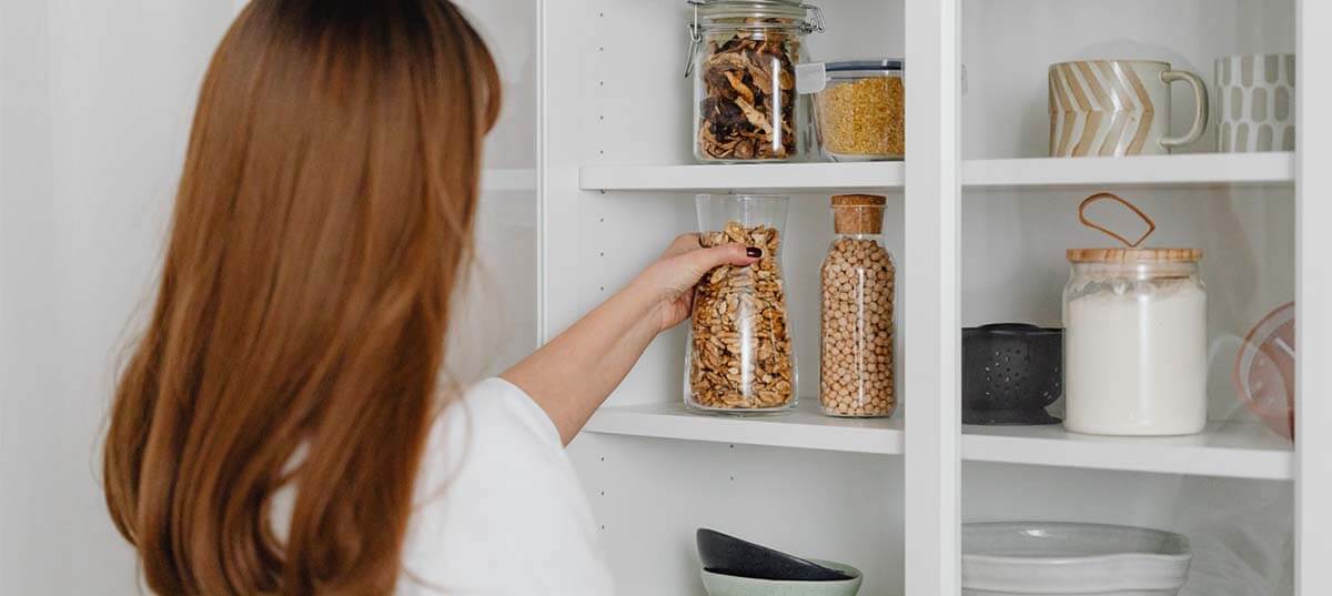 Woman storing pantry items on a shelf. Image credit: Karolina Grabowska