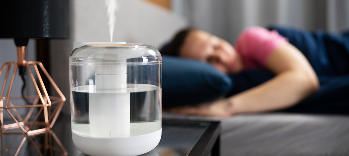 Humidifier on a nightstand next to a sleeping man.