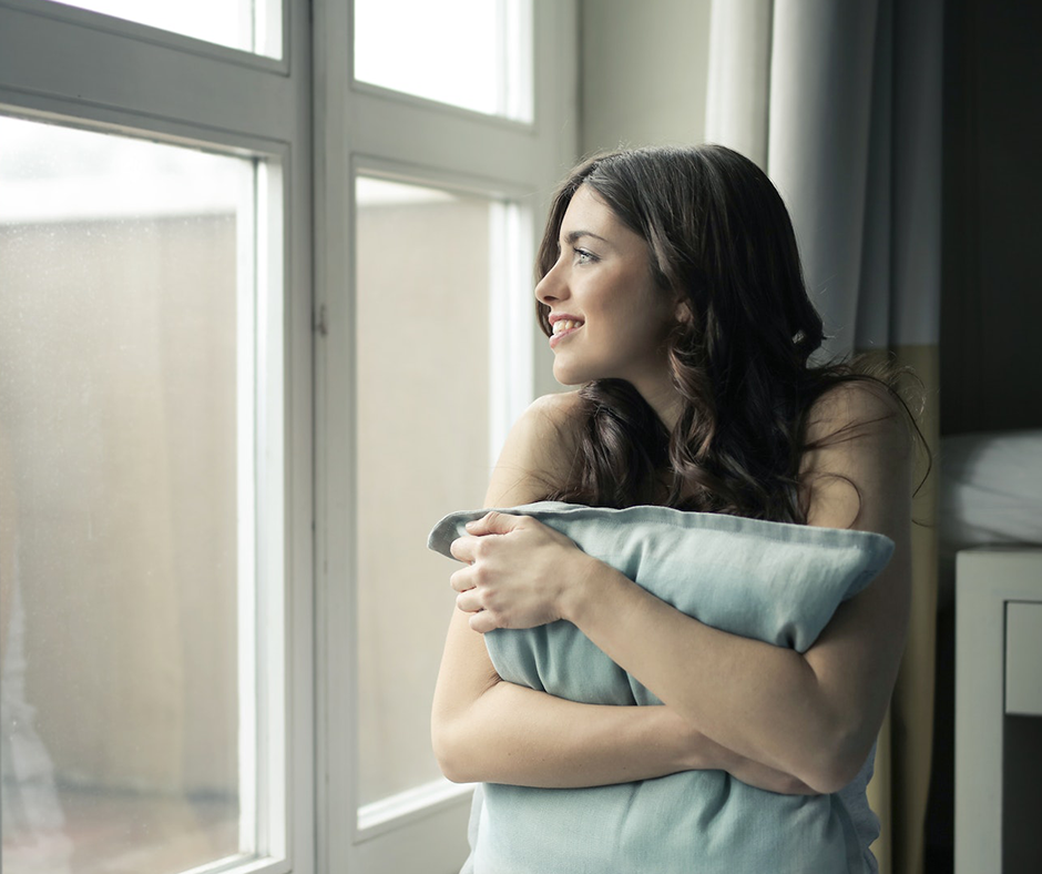 Woman holding a pillow and looking out a window