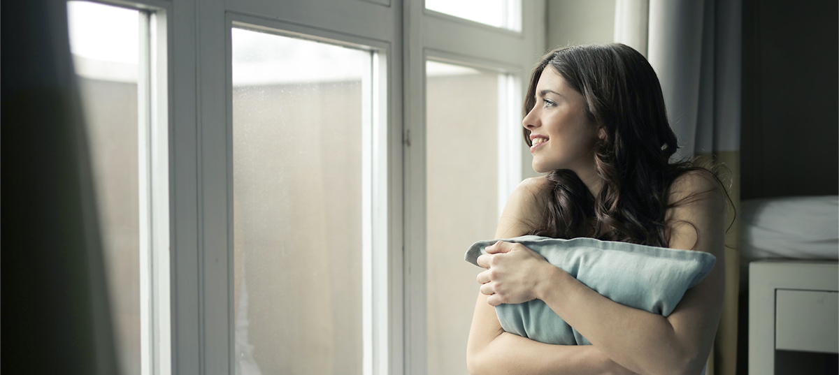 Woman holding a pillow and looking out a window