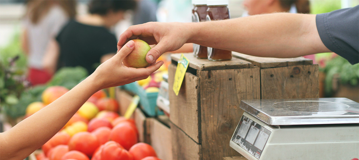 Vendor handing a woman an apple at a farmers market. Image credit: Erik Scheel.