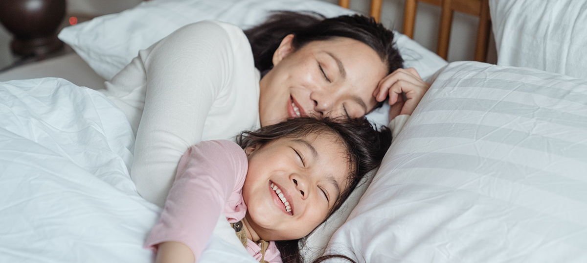 Mother and young daughter cuddling in bed together. Image credit: Ketut Subiyanto.